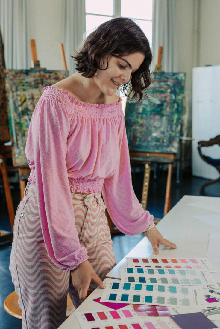 Students with pink blouse stands in front of a workbench on which various cards with color schemes are lying.