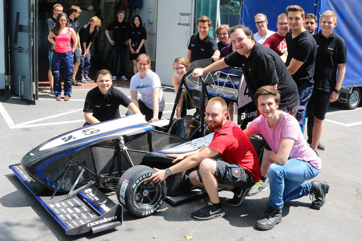 Der neue Rennwagen mit Teilen des Teams vor der Werkstatt. 