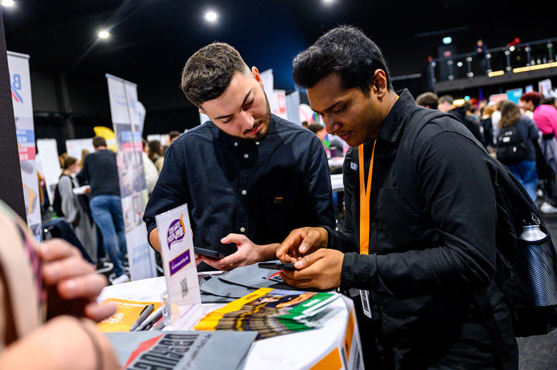 Zwei Personen an einem Standtisch die auf ein Handy gucken