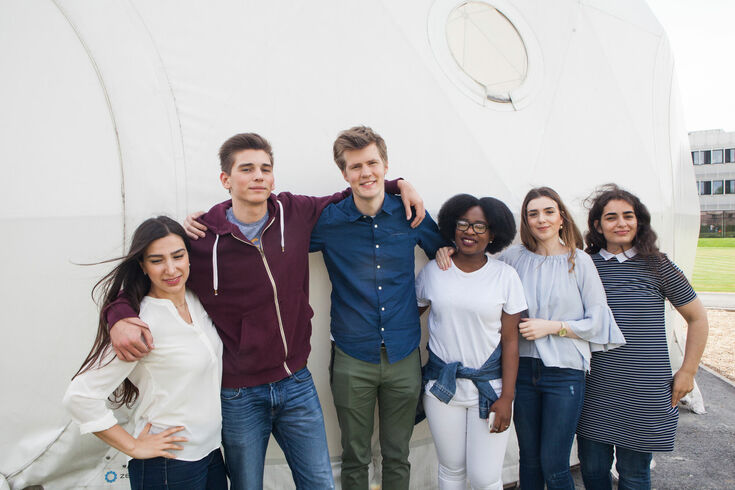 Group of students in front of the zendome on Campus Krefeld-Süd looking into the camera smiling.