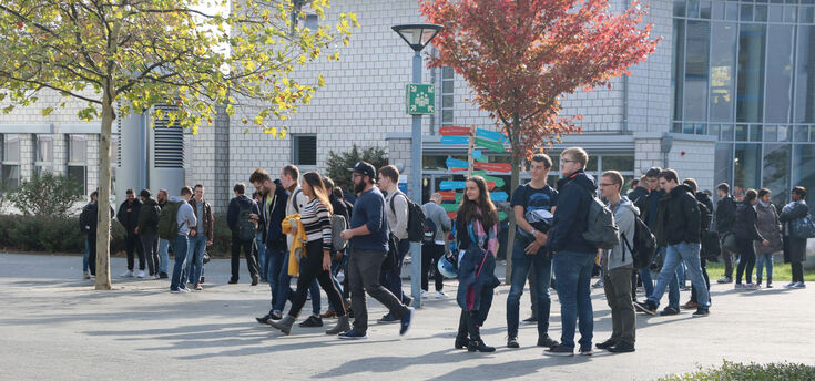 Studierende auf dem Campus vor einem Wegweiser