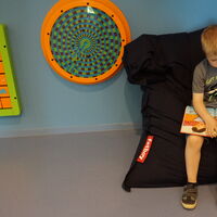 Kind sitzt auf einem Sitzsack und liest ein Buch. Neben dem Kind hängen Spielgeräte an der Wand.