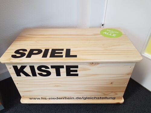 Eine braune Holztruhe mit der Aufschrift "Spiel Kiste"