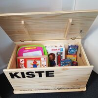 Eine geöffnete Holztruhe, in welcher Kinderspiele liegen.