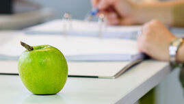 Apfel auf einem Tisch mit einem verschwommenen Ordner und Händen im Hintergrund