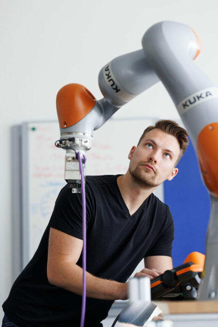 Student in dunklem T-Shirt bedient per Fernbedienung den Arm einer Maschine.