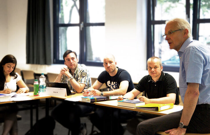 Menschen im Tischkreis mit Lernunterlagen und Mann der redet