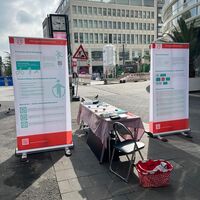 Foto des Stands in der Düsseldorfer Innenstadt. 2 Rollups die links und Rechts von einer Tischreihe mit Infomaterial aufgebaut sind