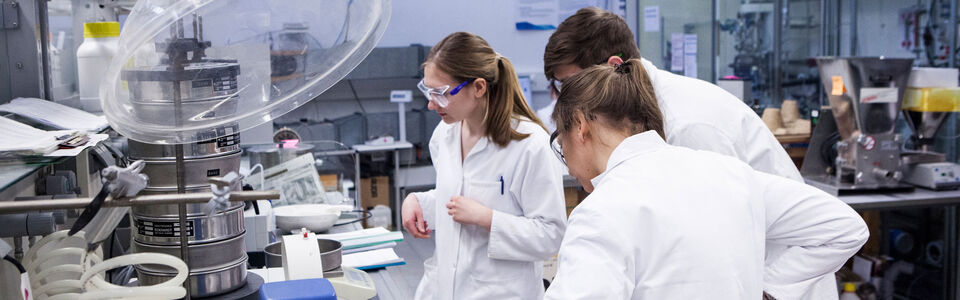 Drei junge Menschen schauen sich eine Probe in einem chemischen Labor an