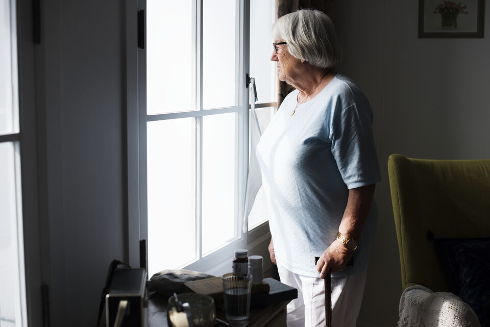 Ältere Frau, die zu Hause am Fenster steht