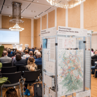 Darstellung der Innenhalle des Events. Menschen die nach vorne schauen.